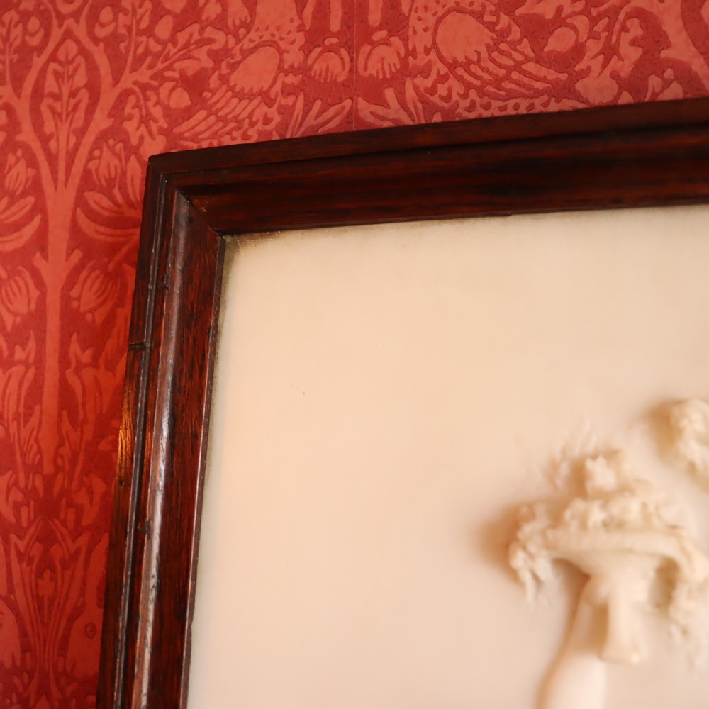 A rectangular dark wood frame enclosing a carved white marble relief sculpture depicting two classical figures in motion. View VIII
