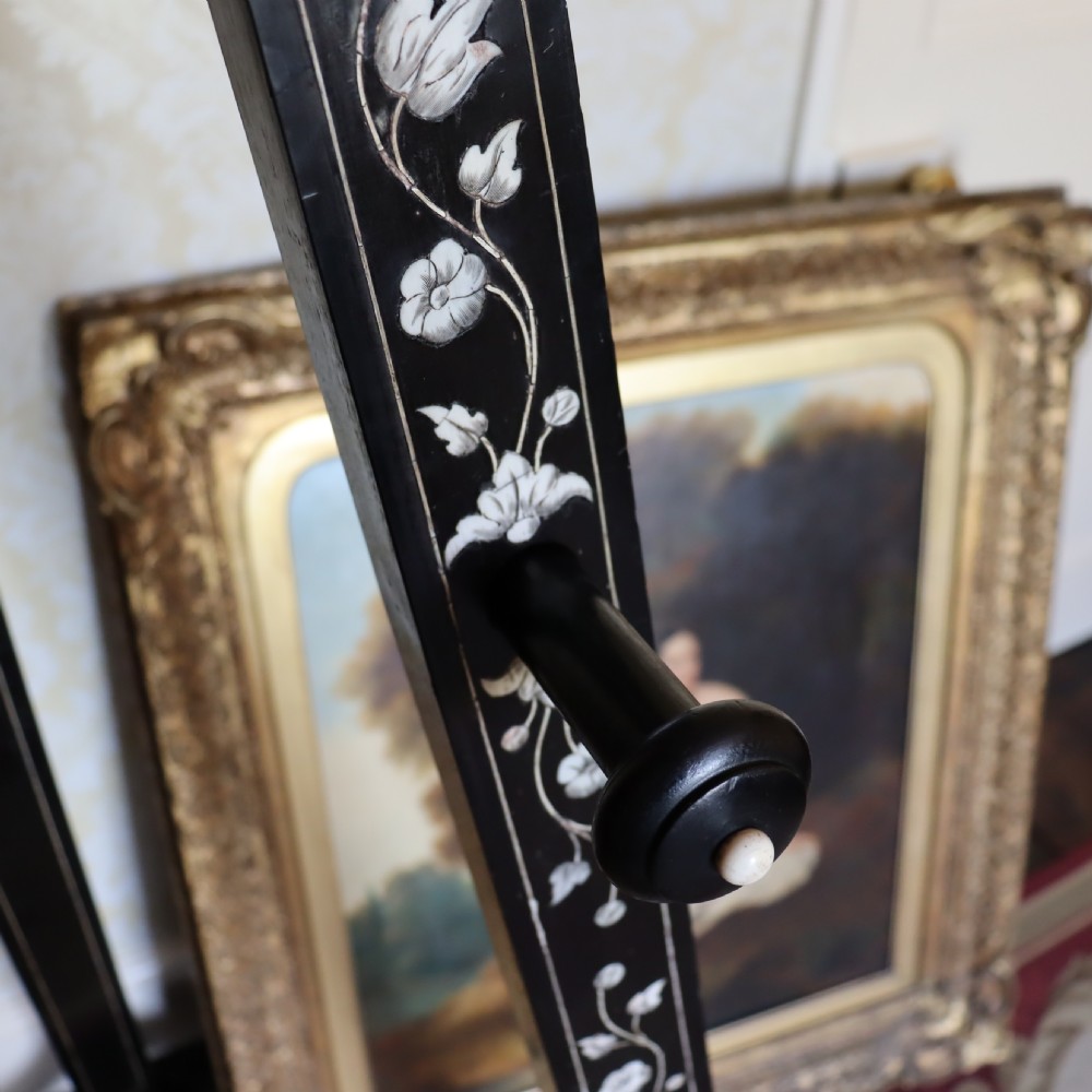 A tall black ebonised gallery easel decorated with white floral inlay along the legs and a carved medallion at the top crest. View VI