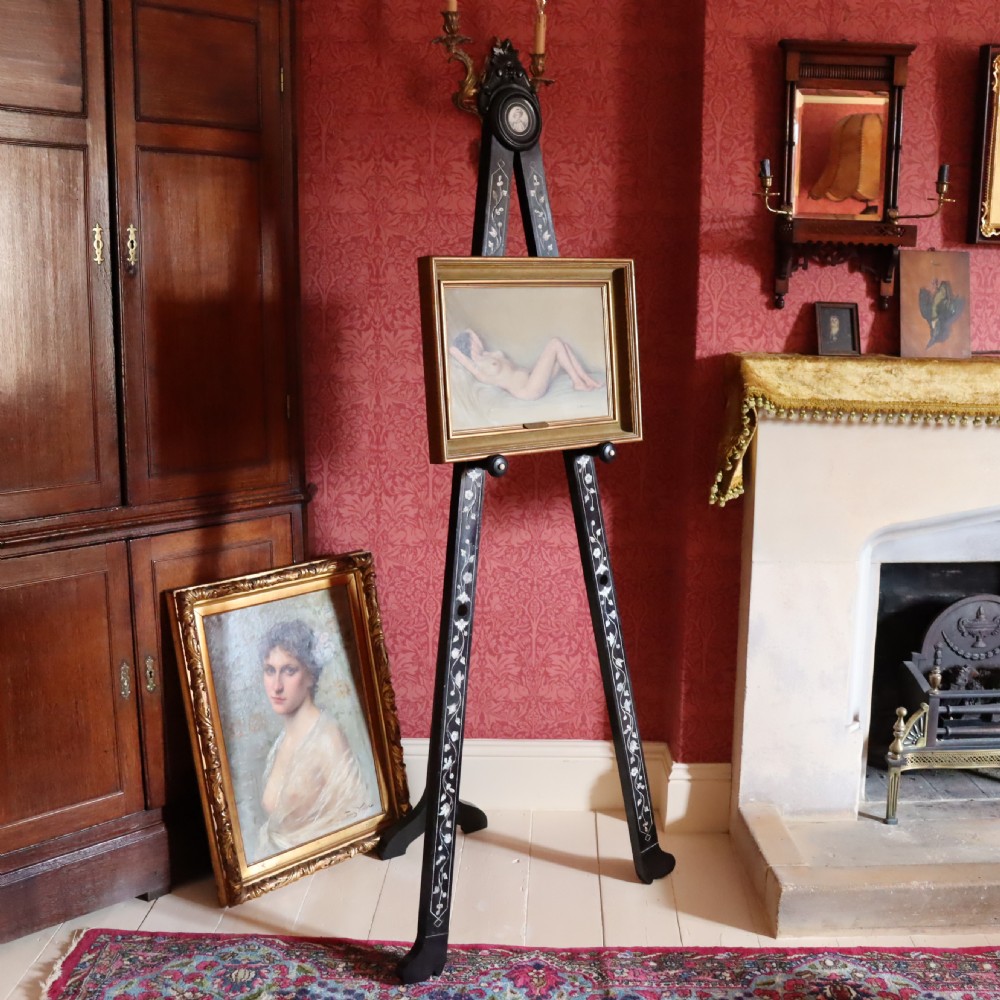 A tall black ebonised gallery easel decorated with white floral inlay along the legs and a carved medallion at the top crest. View VII