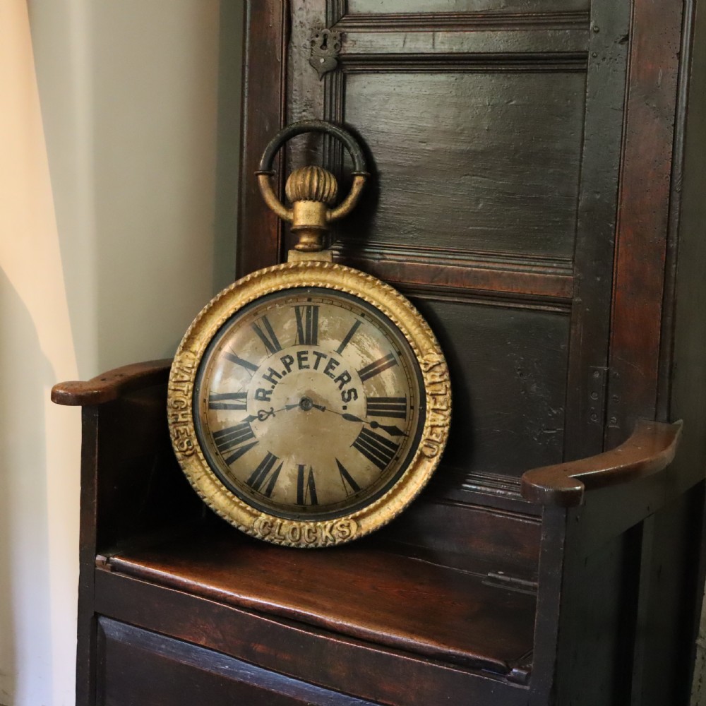 A late 19th-century oversized pocket watch trade sign with a gilded frame, Roman numerals on the dial, and embossed text reading Watches, Jewellery, Clocks.