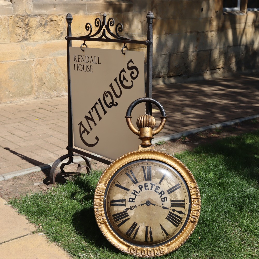 A late 19th-century oversized pocket watch trade sign with a gilded frame, Roman numerals on the dial, and embossed text reading Watches, Jewellery, Clocks. View VI
