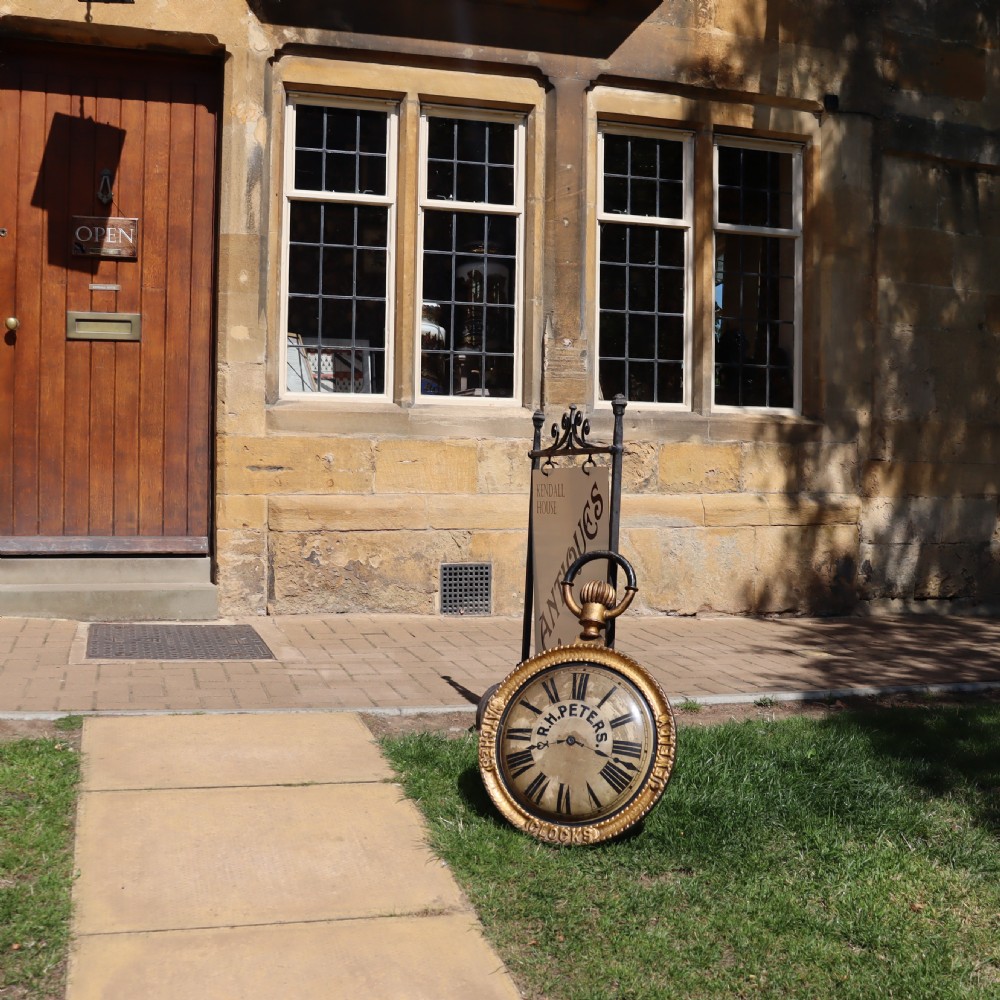 A late 19th-century oversized pocket watch trade sign with a gilded frame, Roman numerals on the dial, and embossed text reading Watches, Jewellery, Clocks. View VII