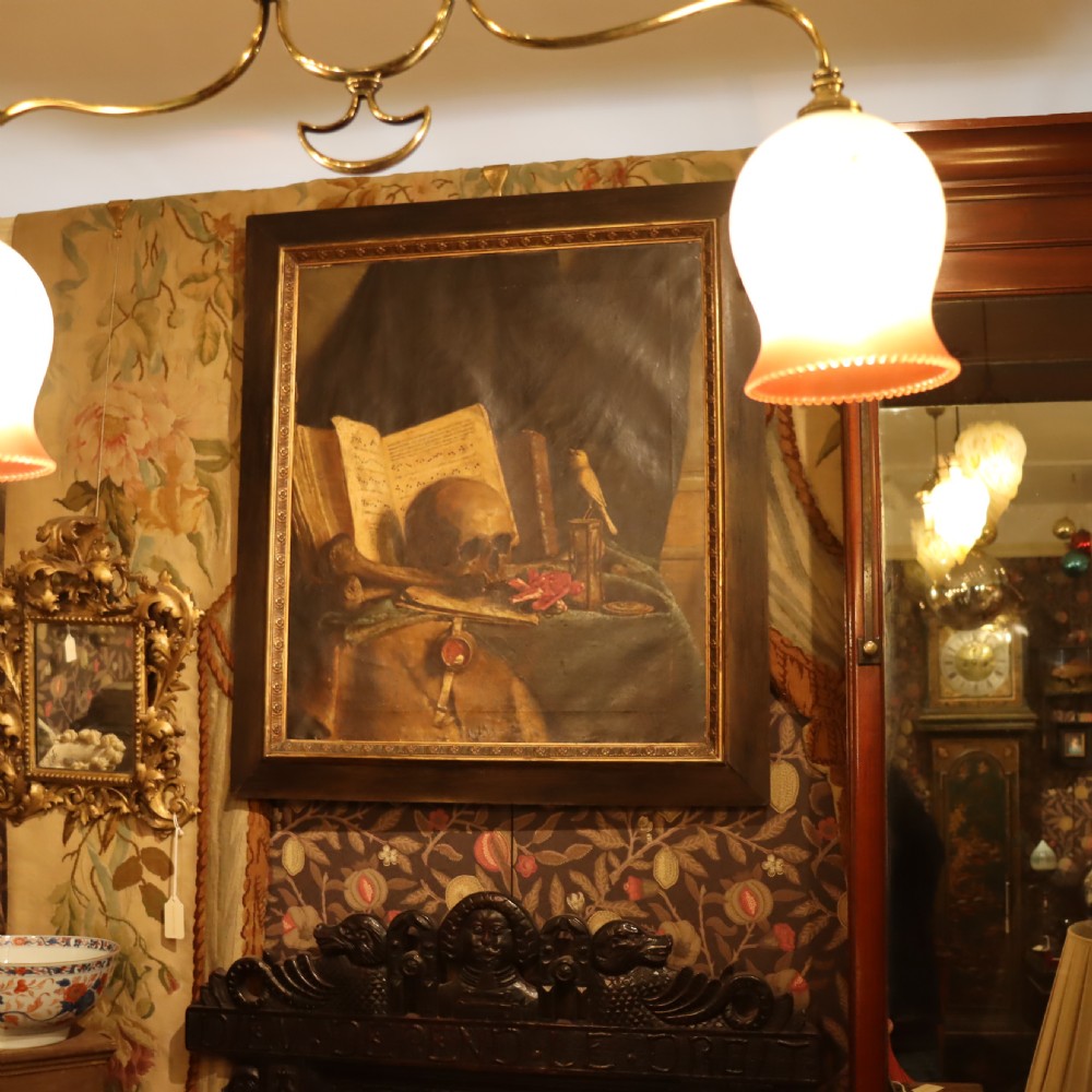An oil painting depicting a vanitas still life with a human skull, open book, and hourglass set inside a dark moulded frame. View IV
