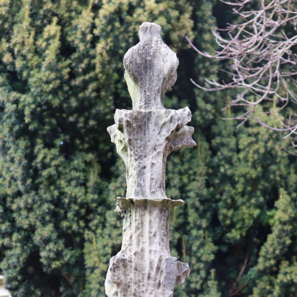 A pair of heavily weathered, hand-carved Gothic limestone pinnacles with intricate crockets and finial tops flanking a stone garden walkway. View V