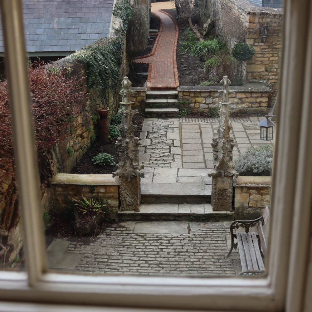 A pair of heavily weathered, hand-carved Gothic limestone pinnacles with intricate crockets and finial tops flanking a stone garden walkway. View VI