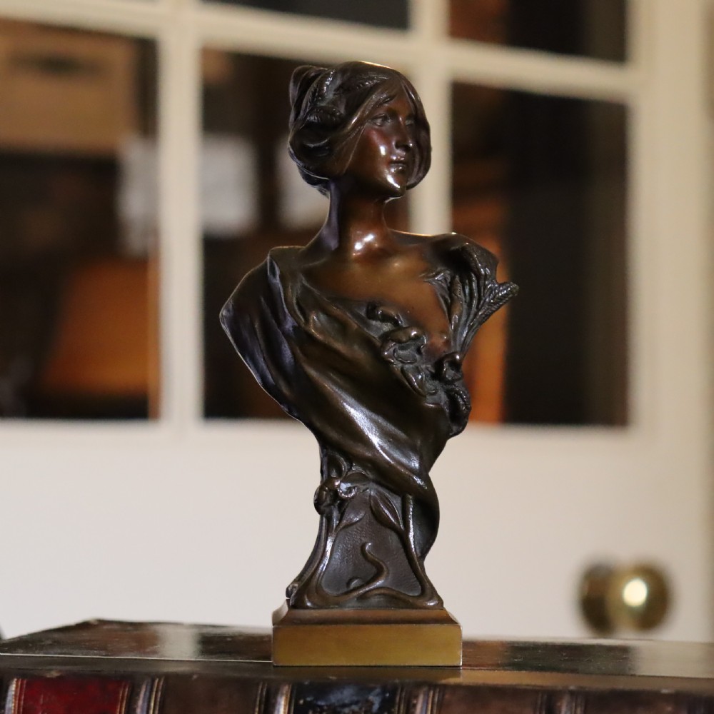An Art Nouveau patinated bronze bust depicting a young woman adorned with ears of wheat and flowing drapery, set on a gilt base. View VII