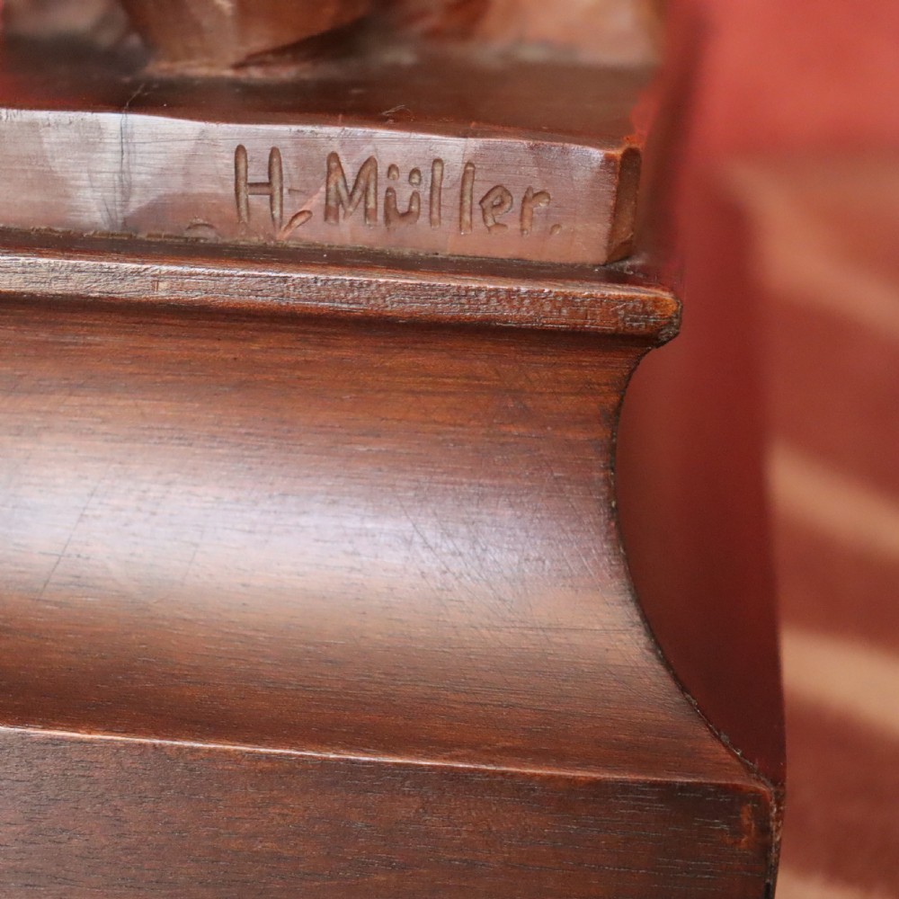 A carved warm brown limewood sculpture depicting a seated female nude figure on a molded rectangular plinth. View V