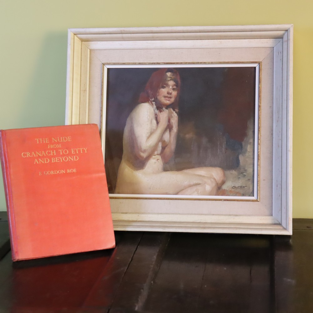 A framed antique oil painting depicting a seated female nude with a red head covering, presented in a light cream moulded wooden frame. View IX