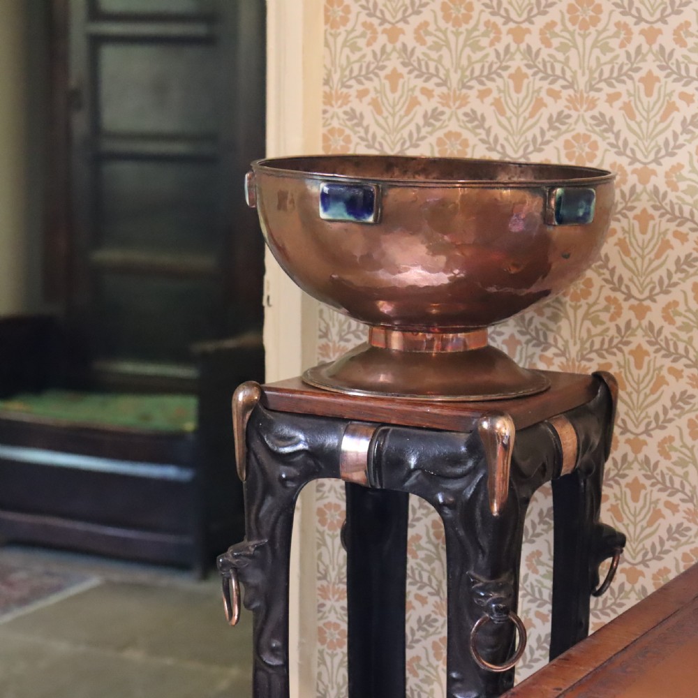 A hand-hammered copper pedestal bowl featuring rectangular blue-glazed ceramic cabochons mounted around the rim. View V