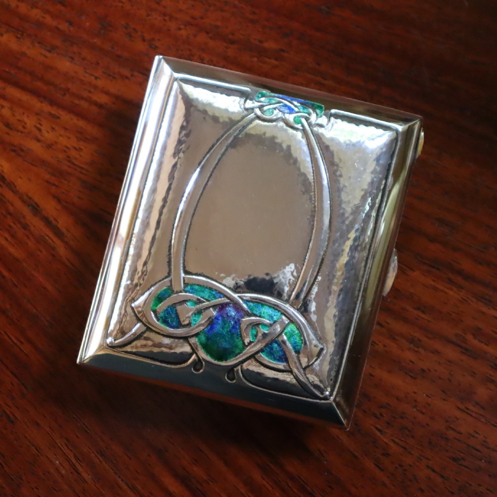 A rectangular planished sterling silver case featuring a raised Celtic knotwork motif filled with vibrant blue and green enamel.