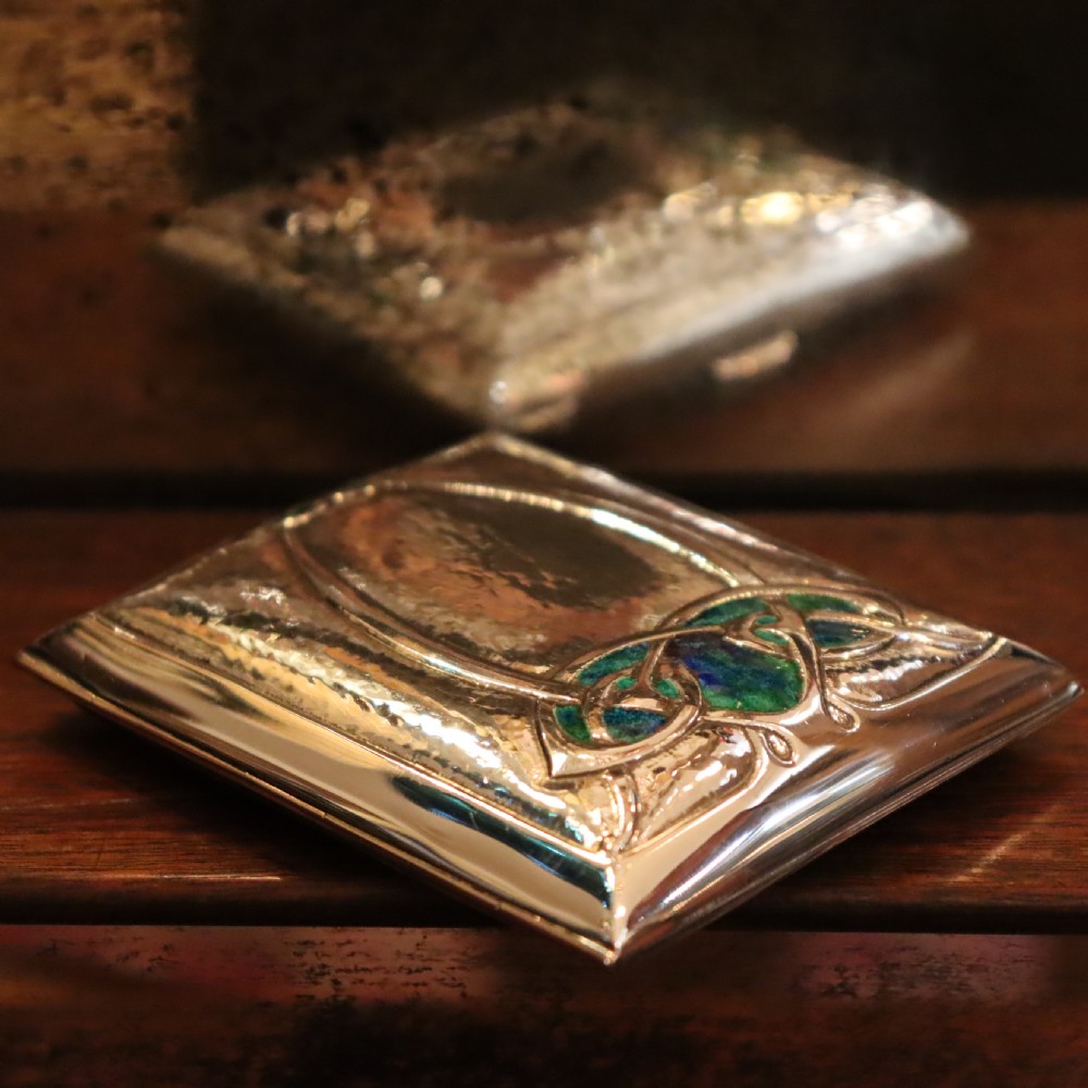 A rectangular planished sterling silver case featuring a raised Celtic knotwork motif filled with vibrant blue and green enamel. View II