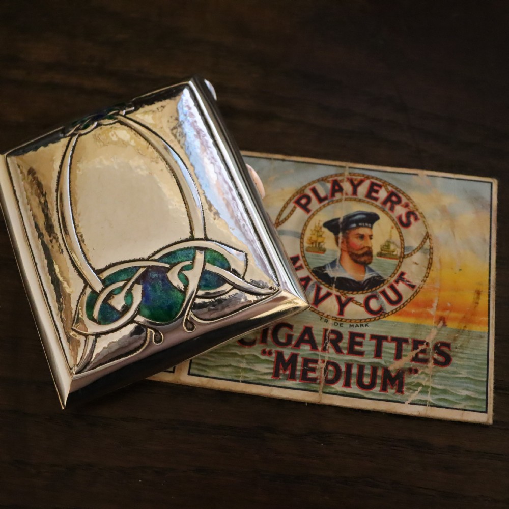 A rectangular planished sterling silver case featuring a raised Celtic knotwork motif filled with vibrant blue and green enamel. View IX