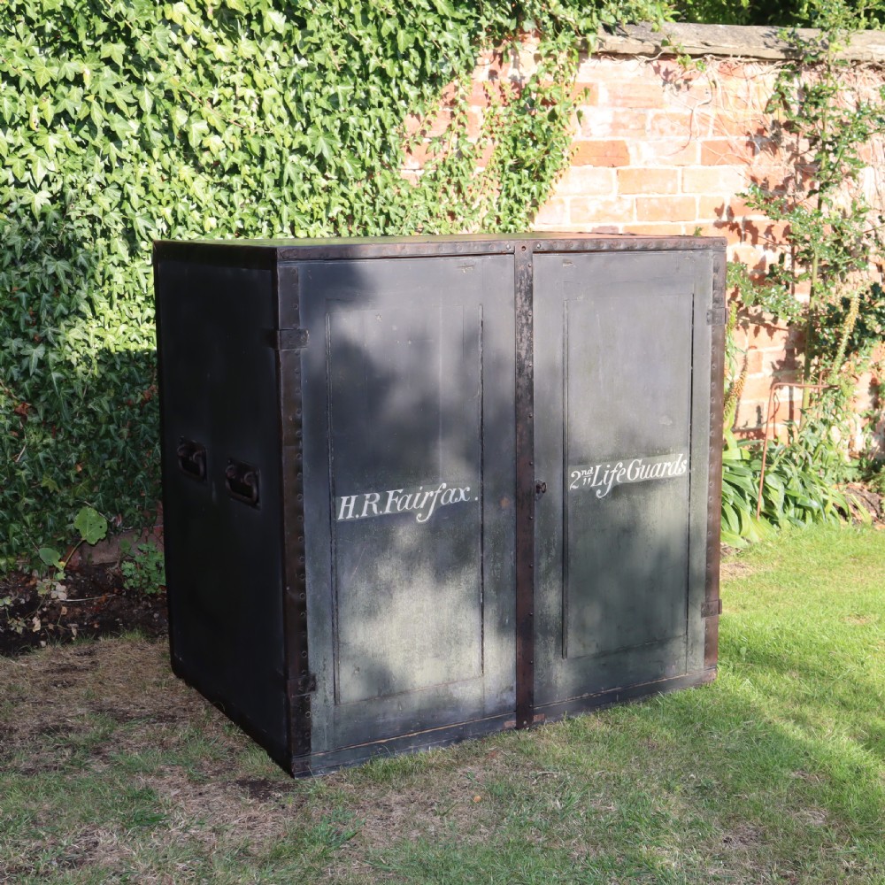A large dark green metal-bound military campaign travelling case with stencilled lettering on the front panels and iron drop handles on the side. View X