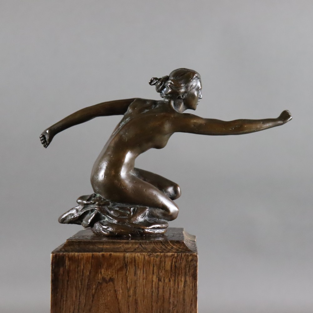 An Art Deco dark bronze sculpture of a kneeling nude woman reaching forward, mounted on a rustic square timber base. View III