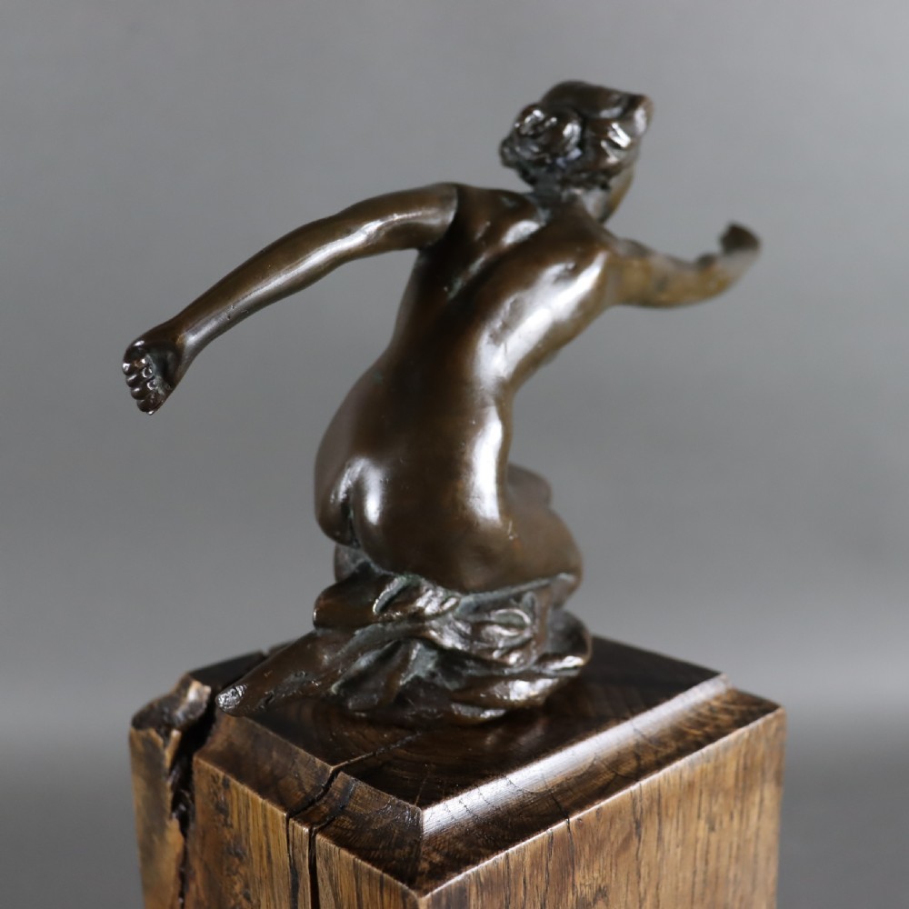 An Art Deco dark bronze sculpture of a kneeling nude woman reaching forward, mounted on a rustic square timber base. View IV