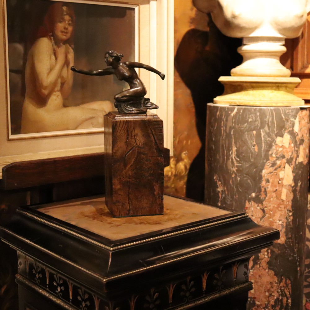 An Art Deco dark bronze sculpture of a kneeling nude woman reaching forward, mounted on a rustic square timber base. View VII
