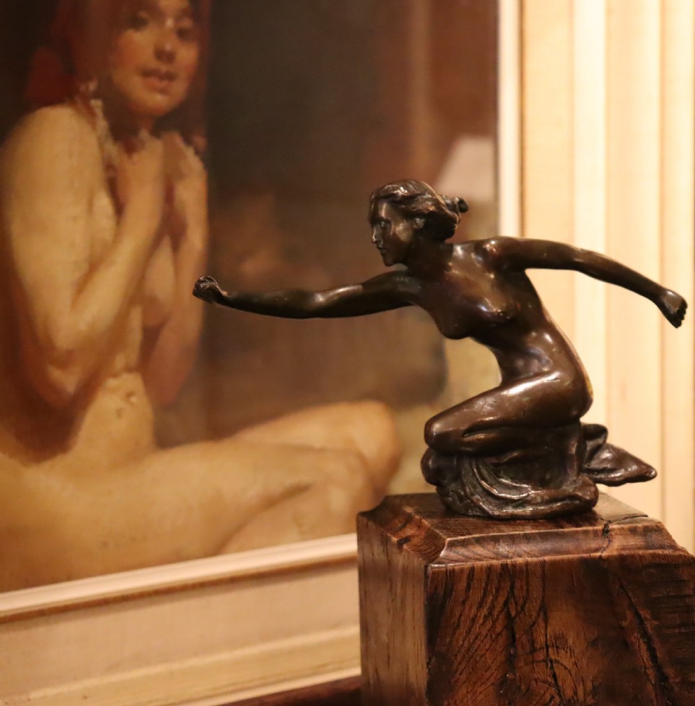 An Art Deco dark bronze sculpture of a kneeling nude woman reaching forward, mounted on a rustic square timber base. View VIII