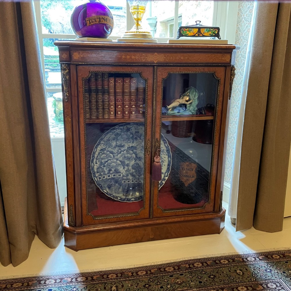 A Victorian burr walnut pier cabinet with two glazed doors, marquetry crossbanding along the frieze, and brass mounts.