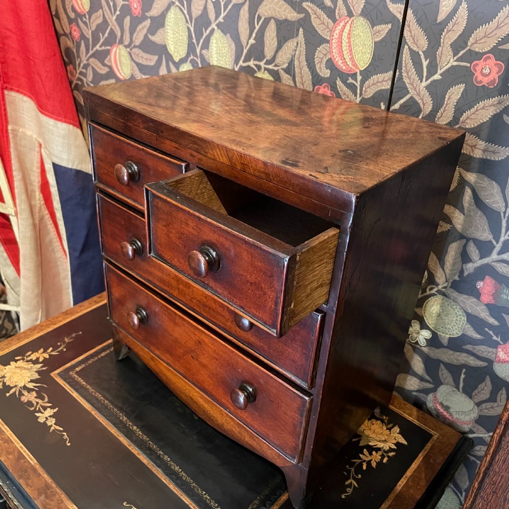 A Georgian mahogany miniature apprentice chest of drawers with turned wooden handles, four graduated drawers, and bracket feet.