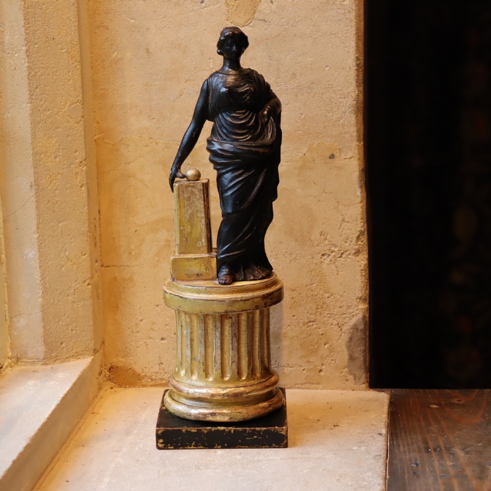 A dark ebonised carved wood figure of the classical goddess Fortuna set atop a gilded fluted column pedestal and square base.