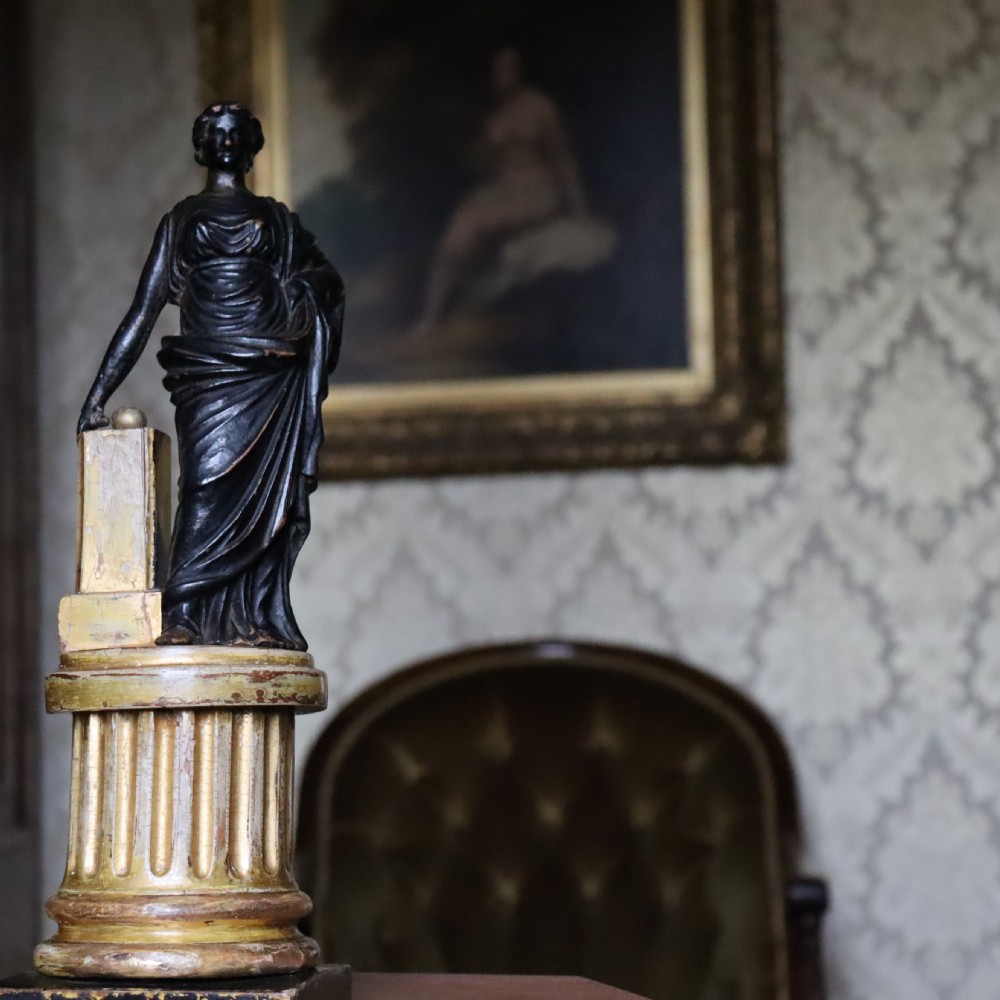 A dark ebonised carved wood figure of the classical goddess Fortuna set atop a gilded fluted column pedestal and square base. View IX
