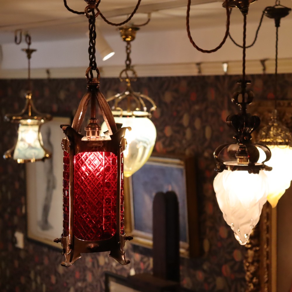 An Arts and Crafts copper hanging lantern fitted with a diamond-moulded cranberry red glass shade. View III