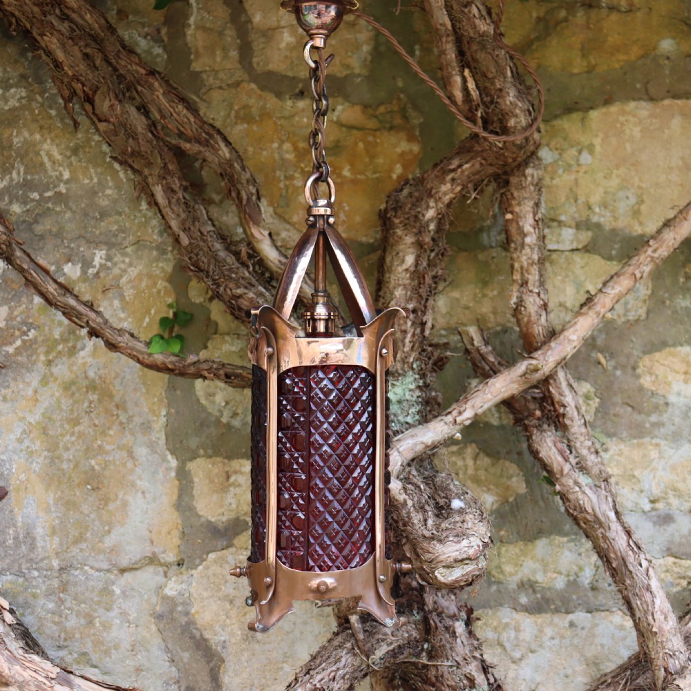 An Arts and Crafts copper hanging lantern fitted with a diamond-moulded cranberry red glass shade.