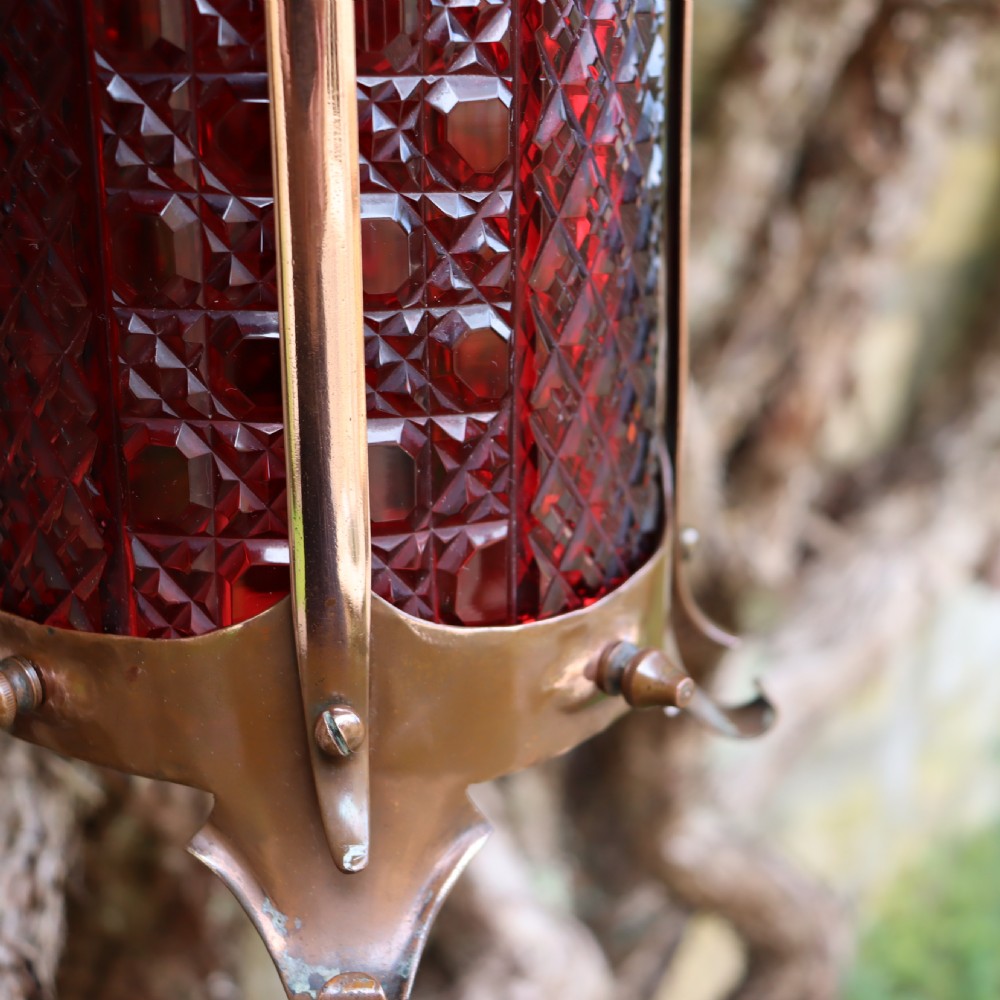 An Arts and Crafts copper hanging lantern fitted with a diamond-moulded cranberry red glass shade. View IV