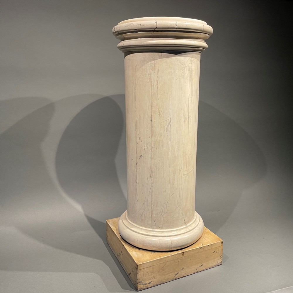 A painted off-white Victorian turned wooden column with a circular molded capital and base resting on a square wooden plinth.