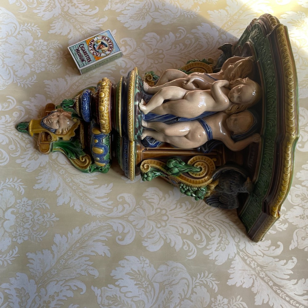 A Victorian Minton majolica wall bracket featuring three sculpted cherubs supporting a green glaze top shelf above a mascaron base. View V
