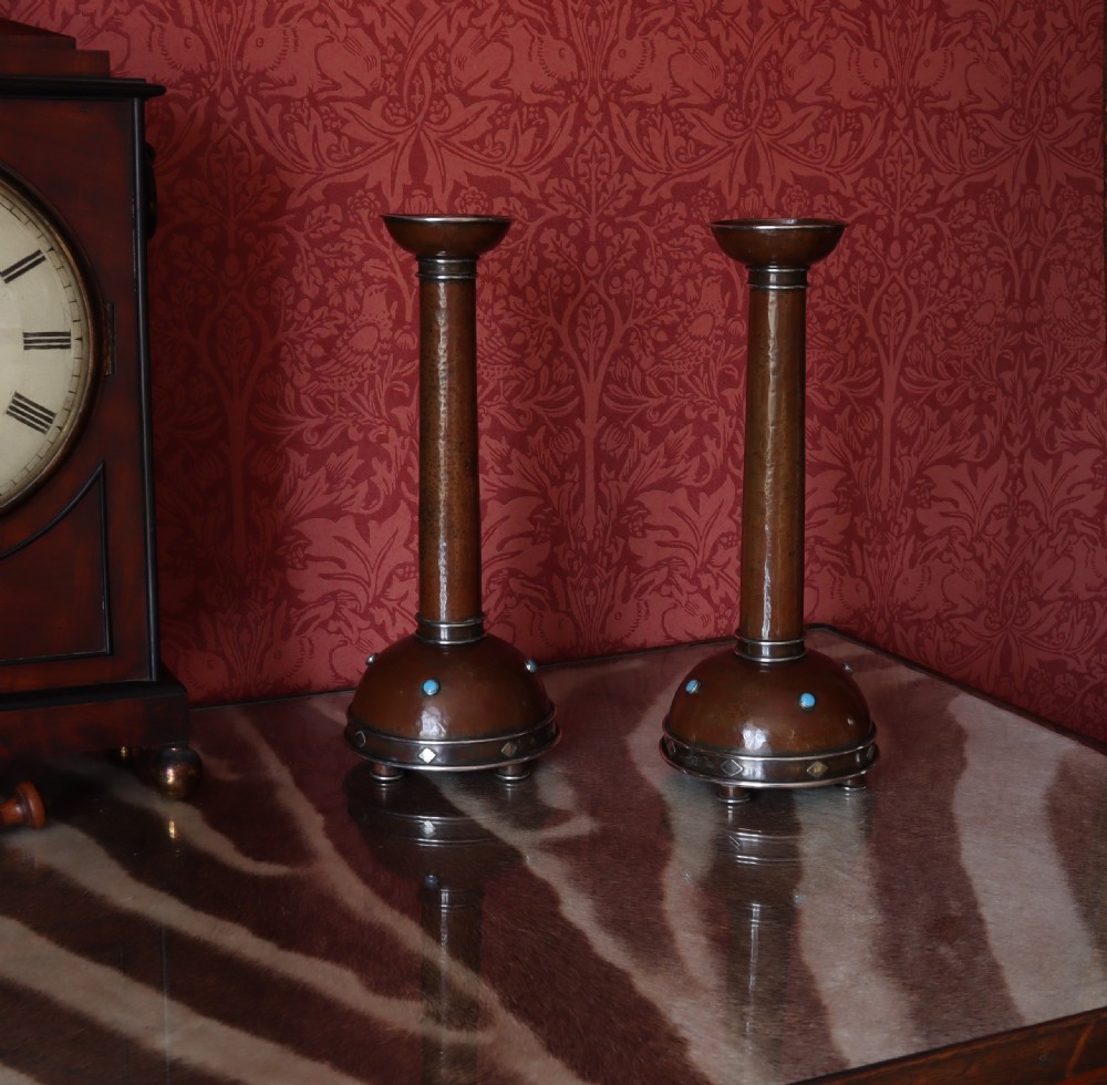 A pair of tall Arts and Crafts hammered copper candlesticks featuring domed bases inlaid with turquoise cabochons and silver detail. View IX
