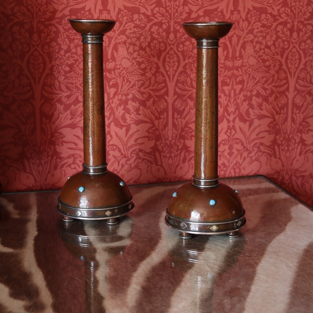 A pair of tall Arts and Crafts hammered copper candlesticks featuring domed bases inlaid with turquoise cabochons and silver detail. View II
