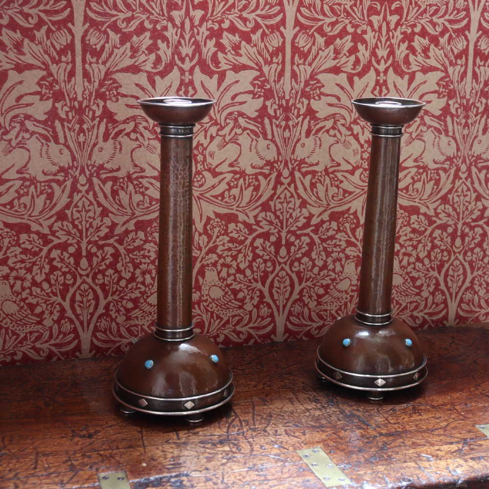 A pair of tall Arts and Crafts hammered copper candlesticks featuring domed bases inlaid with turquoise cabochons and silver detail. View IV