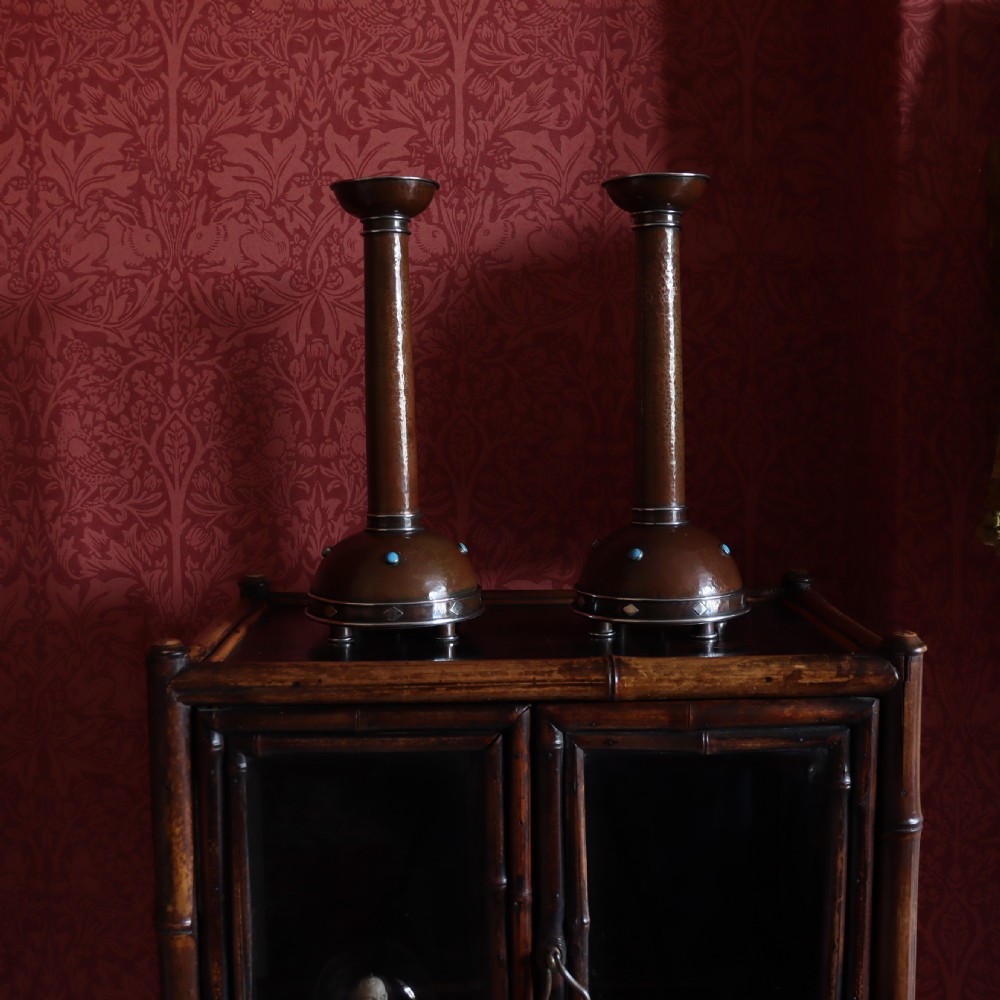 A pair of tall Arts and Crafts hammered copper candlesticks featuring domed bases inlaid with turquoise cabochons and silver detail. View V