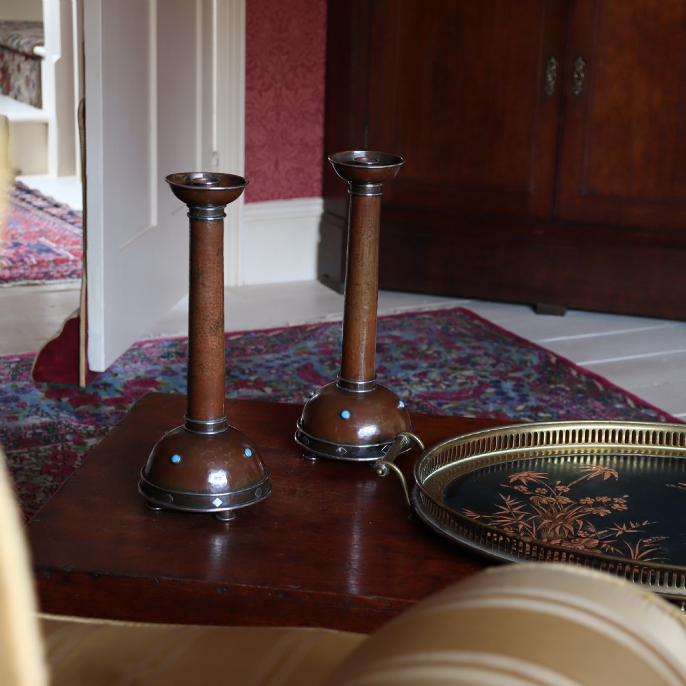 A pair of tall Arts and Crafts hammered copper candlesticks featuring domed bases inlaid with turquoise cabochons and silver detail. View VI