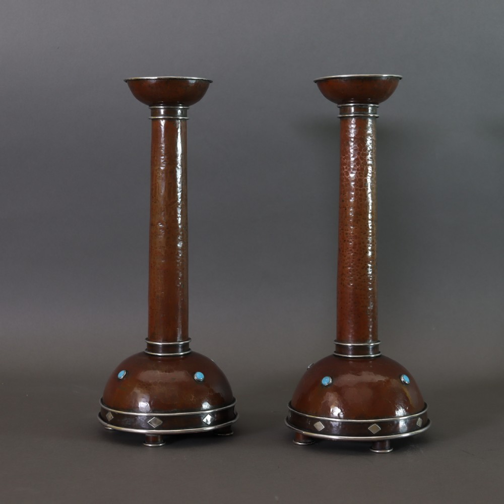 A pair of tall Arts and Crafts hammered copper candlesticks featuring domed bases inlaid with turquoise cabochons and silver detail.
