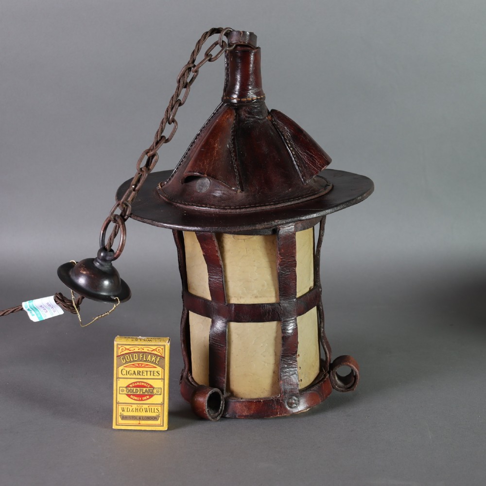 An Arts and Crafts ceiling lantern made of dark chestnut brown hand-stitched leather straps surrounding translucent vellum panels, suspended by a metal chain. View V
