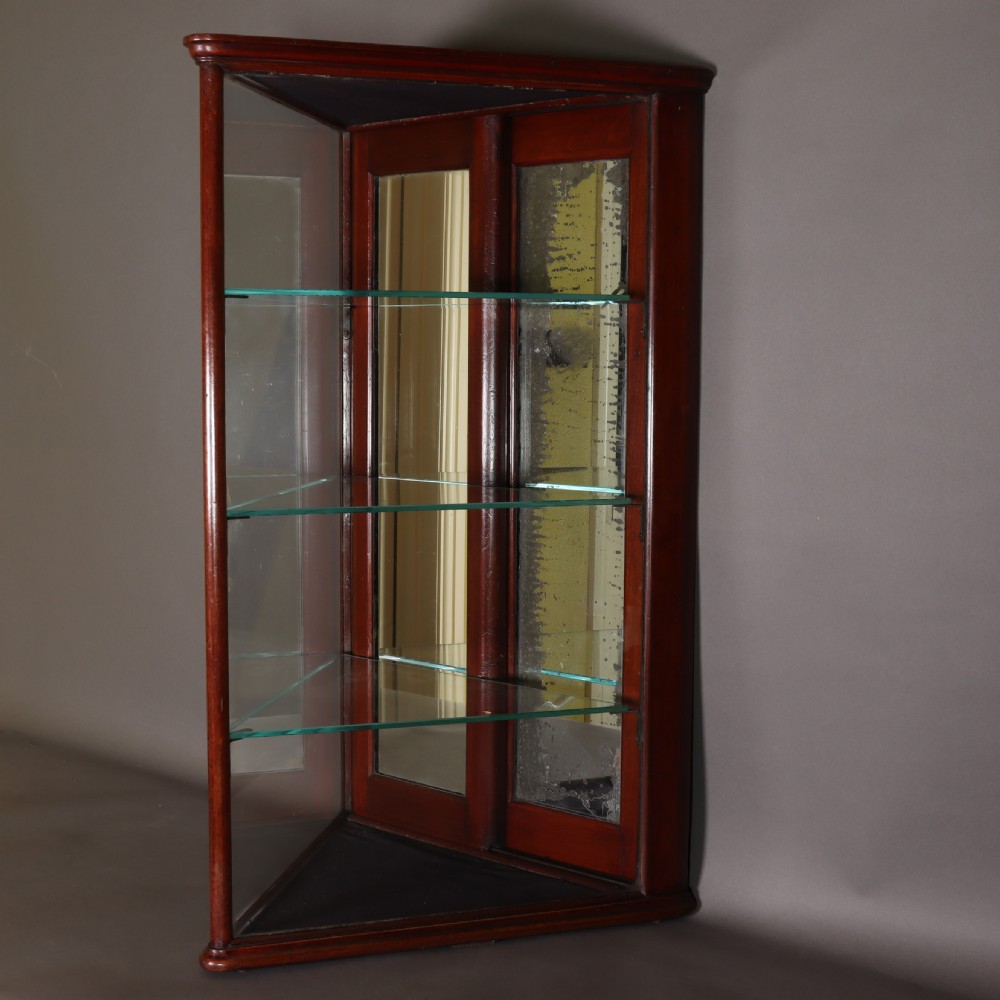 A Victorian mahogany and glass corner display cabinet featuring three glass shelves and mirrored back doors.