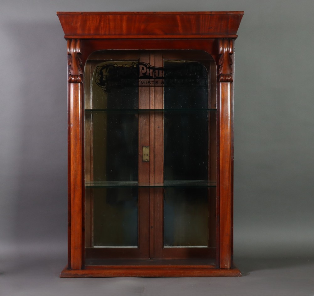 A Victorian mahogany pharmacy display cabinet featuring carved side columns, glass shelves, and gilded glass lettering reading Kemps Pharmacy Chemist and Opticians.