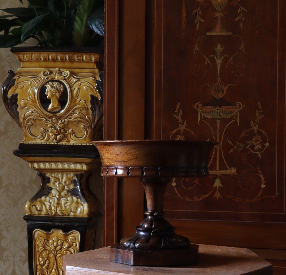 A dark rosewood tazza urn featuring a circular flared rim with an integrated brass liner, supported by a turned pedestal on an octagonal wooden base. View VI