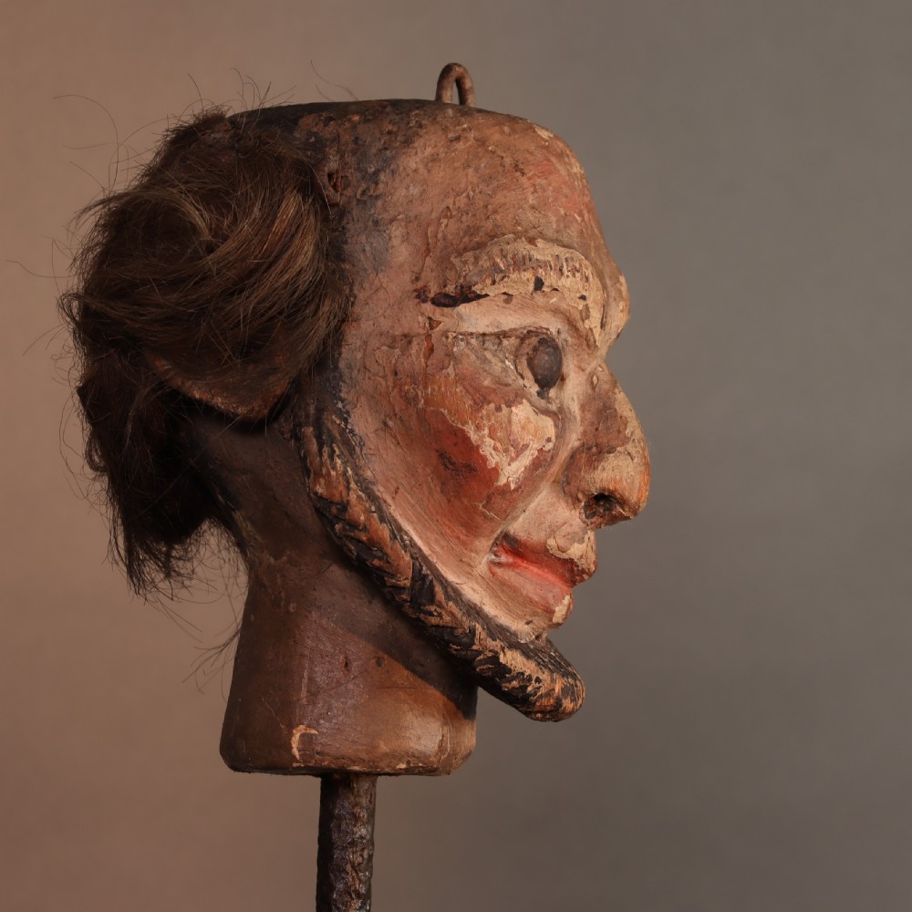 A nineteenth-century carved and polychrome painted wooden puppet head featuring natural hair and a bearded face, displayed on a metal stand. View III