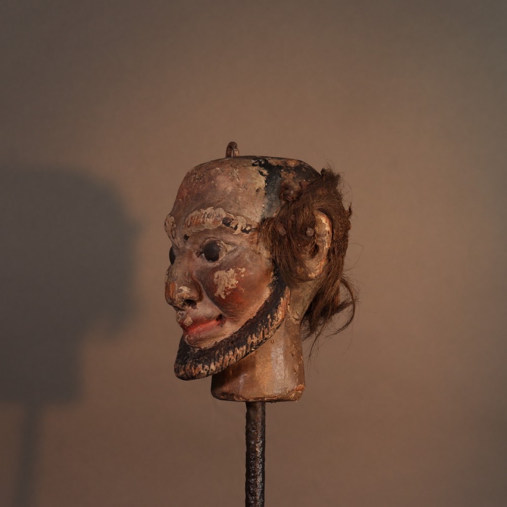 A nineteenth-century carved and polychrome painted wooden puppet head featuring natural hair and a bearded face, displayed on a metal stand. View IV