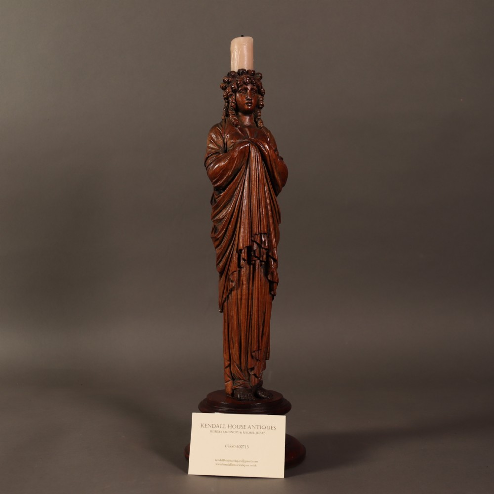 A 19th-century carved wooden candlestick shaped as a draped female figure standing on a round turned socle base. View V