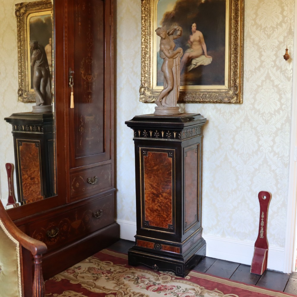 An ebonised Victorian Aesthetic Movement display pedestal featuring inset burr walnut panels, gilt incised frieze detailing, and a moulded square top. View II