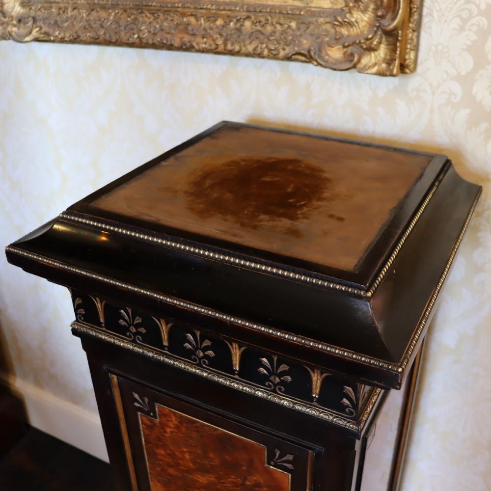 An ebonised Victorian Aesthetic Movement display pedestal featuring inset burr walnut panels, gilt incised frieze detailing, and a moulded square top. View V