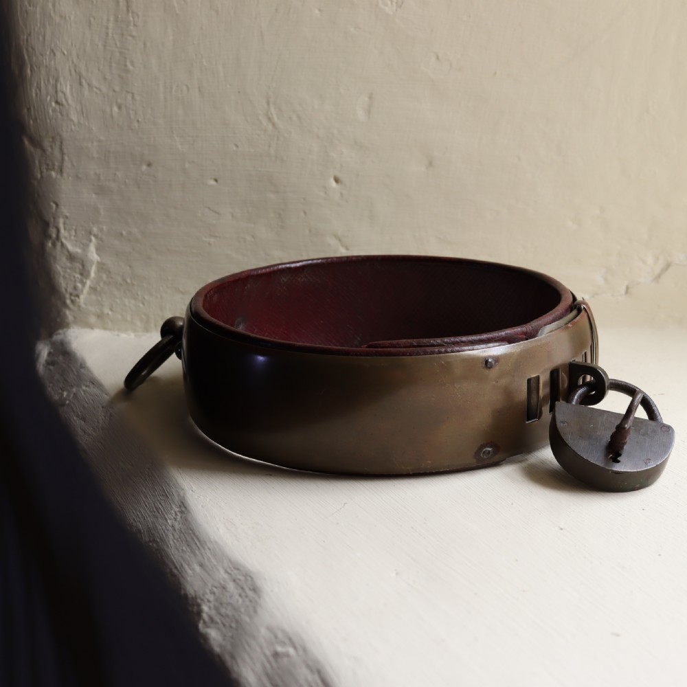 A heavy early nineteenth century bevelled brass dog collar lined with red leather and secured with a brass padlock and key. View III