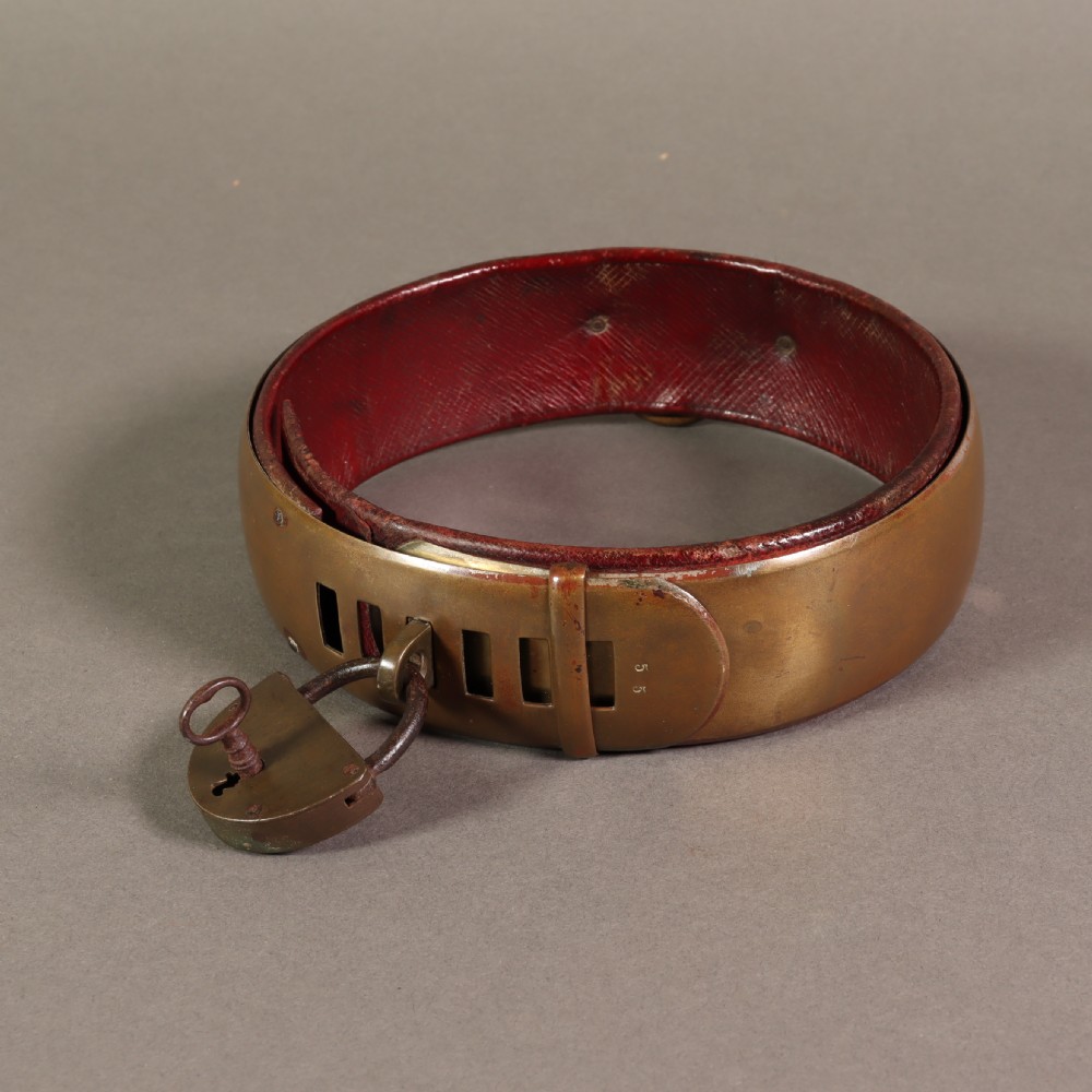 A heavy early nineteenth century bevelled brass dog collar lined with red leather and secured with a brass padlock and key.