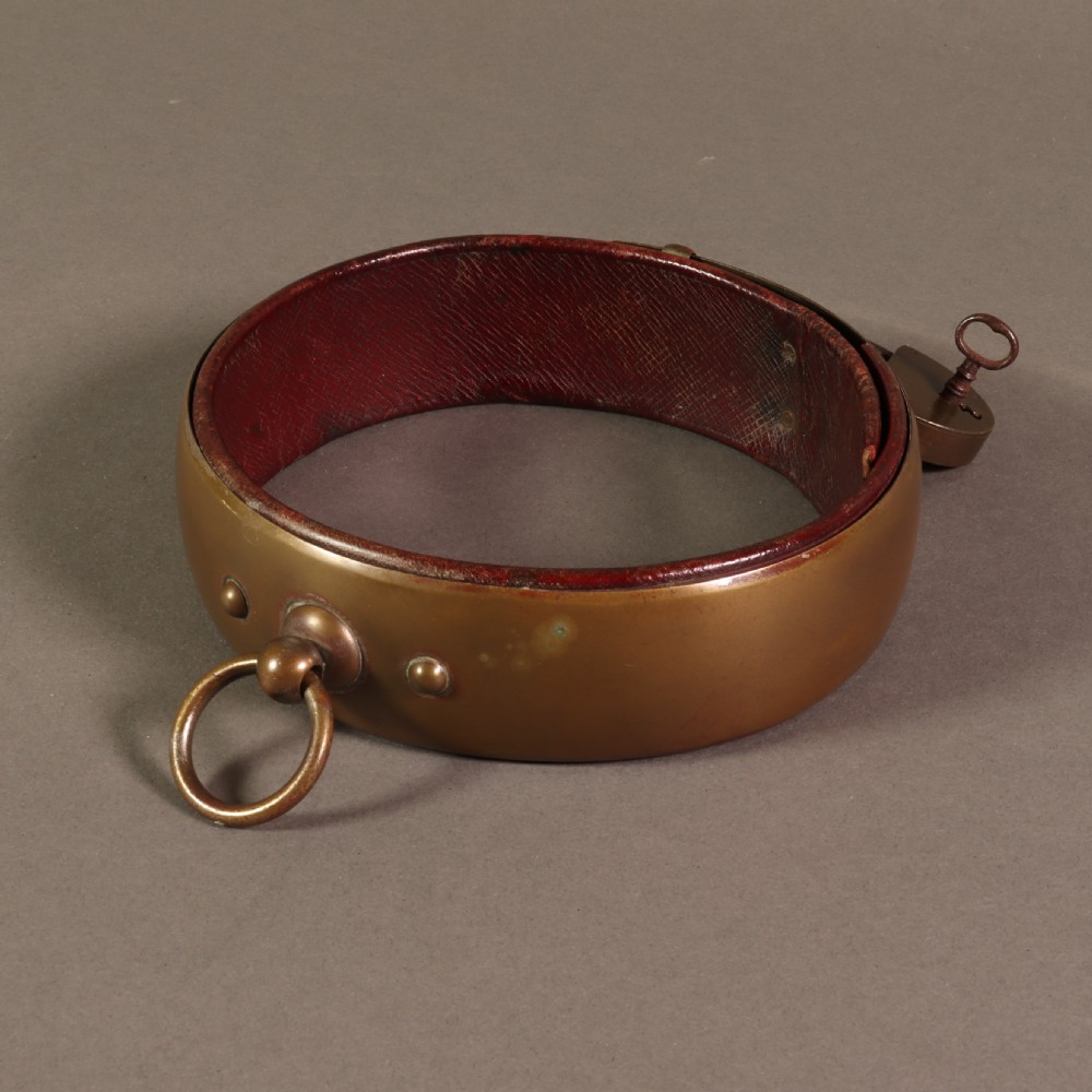 A heavy early nineteenth century bevelled brass dog collar lined with red leather and secured with a brass padlock and key. View V