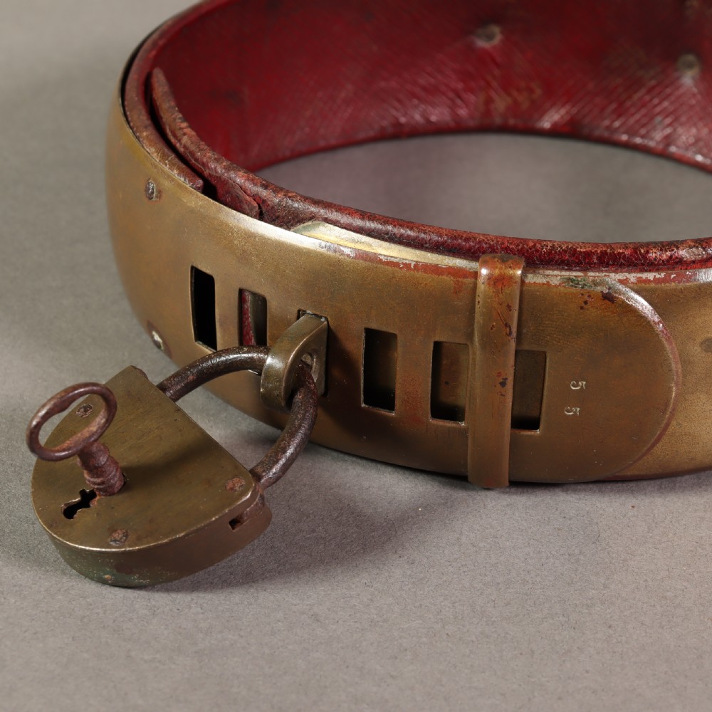 A heavy early nineteenth century bevelled brass dog collar lined with red leather and secured with a brass padlock and key. View VI