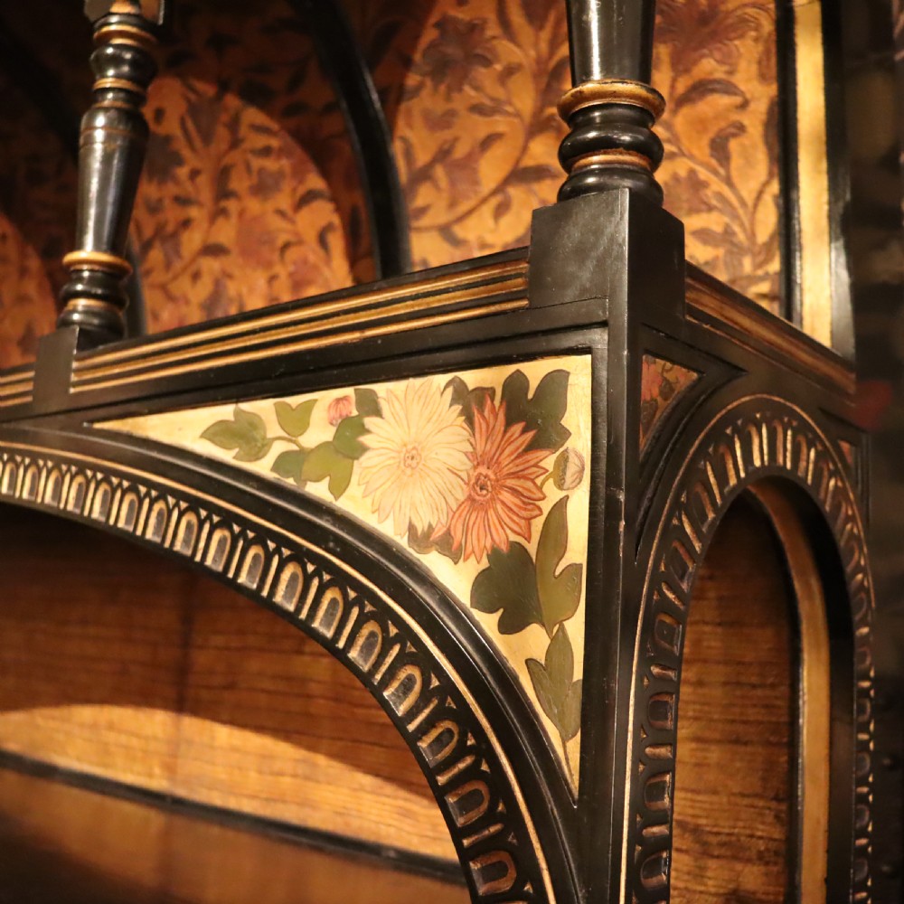 An Aesthetic Movement ebonised mahogany display cabinet featuring gilt highlights, turned spindle arcades, painted floral panels, and mirrored doors. View V